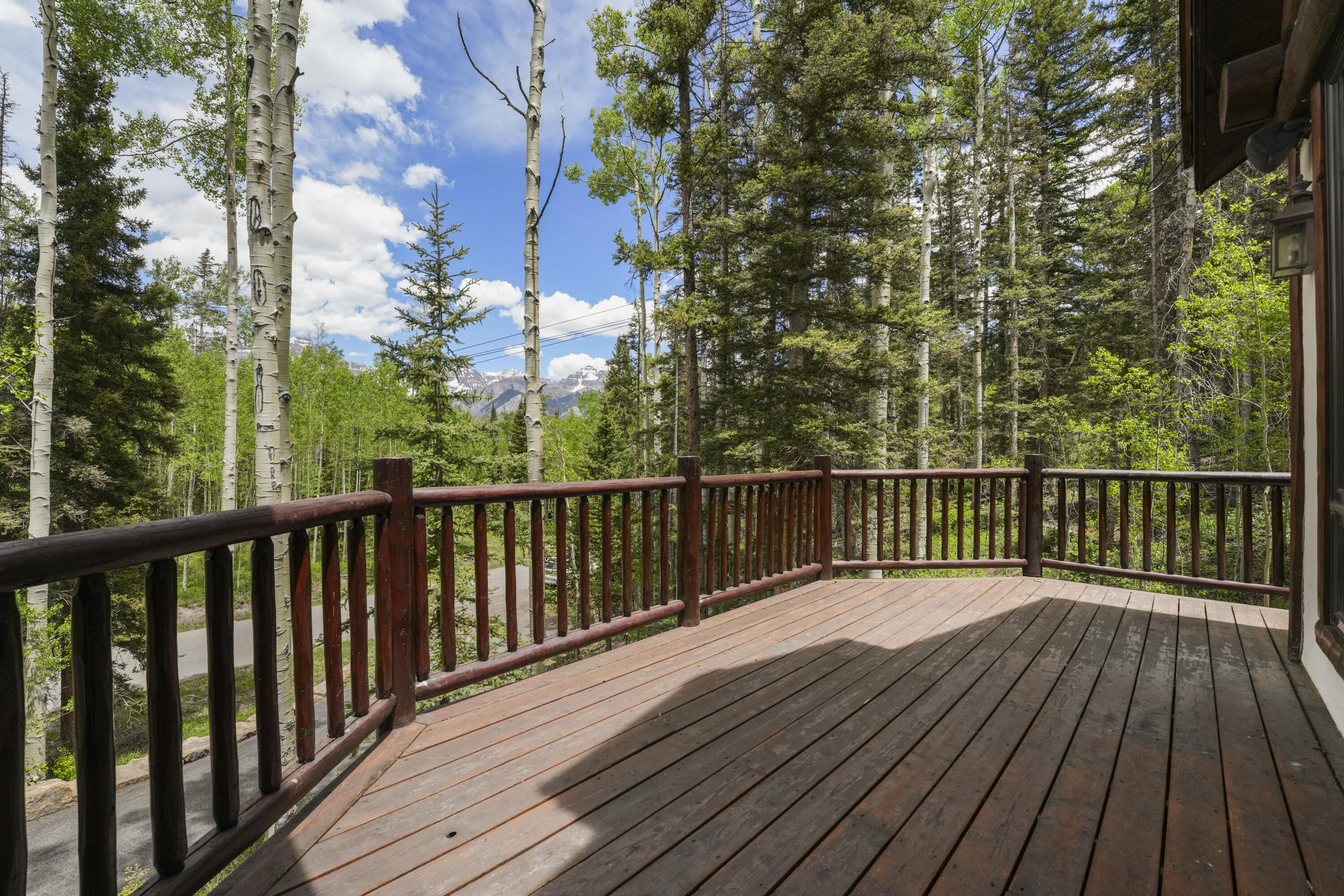 Wooden deck overlooking aspen and evergreen forest with distant snow-dusted mountain peaks.