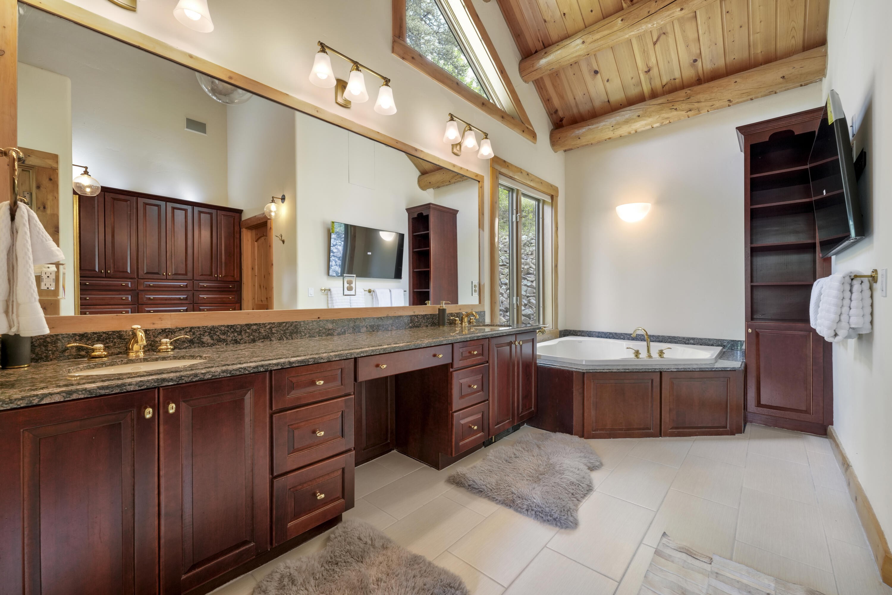 Bathroom with a dark wood double vanity, corner soaking tub, and vaulted timber ceiling.