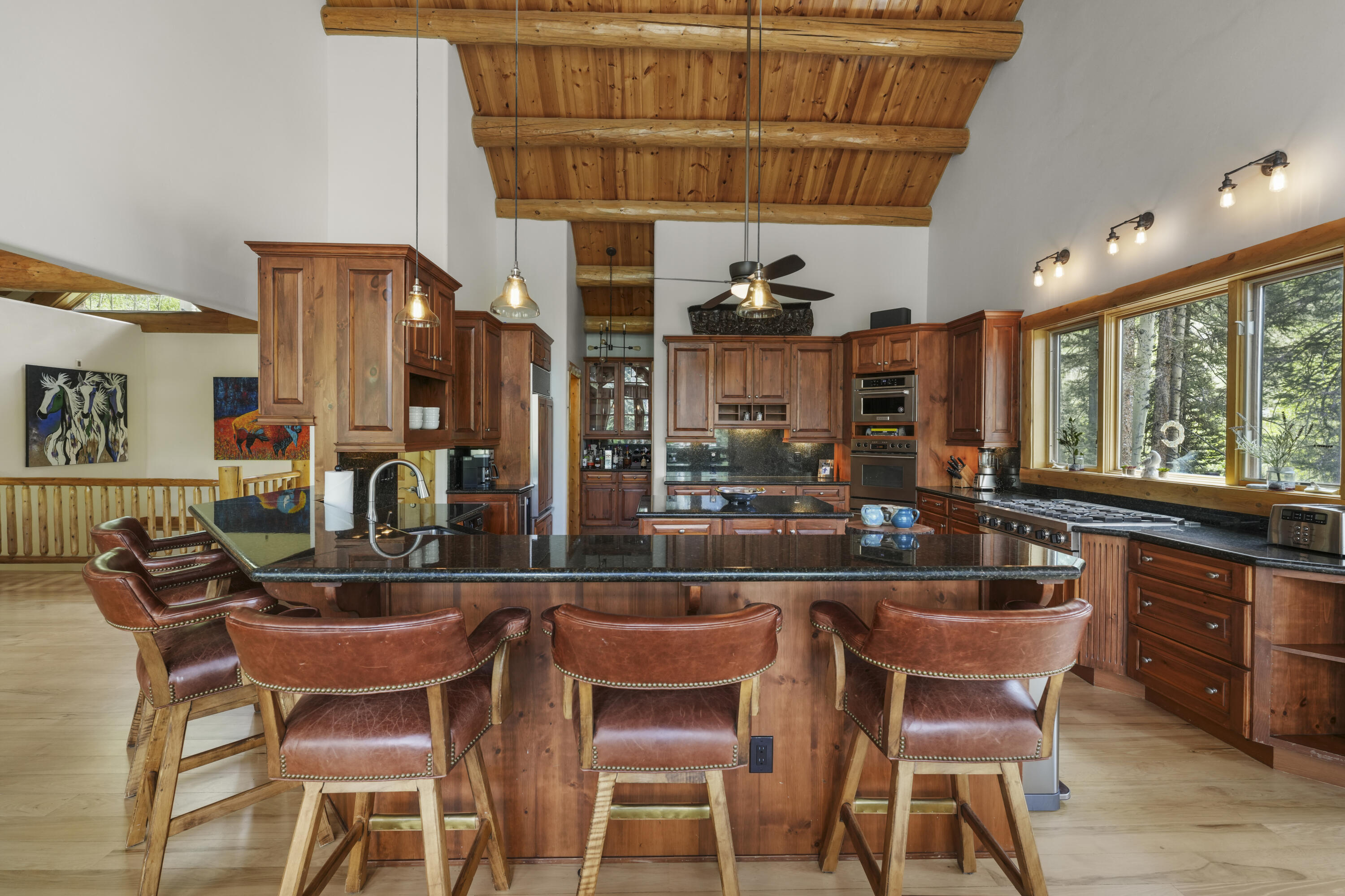 Kitchen with a large granite island, leather bar stools, wood cabinetry and exposed timber ceiling beams.