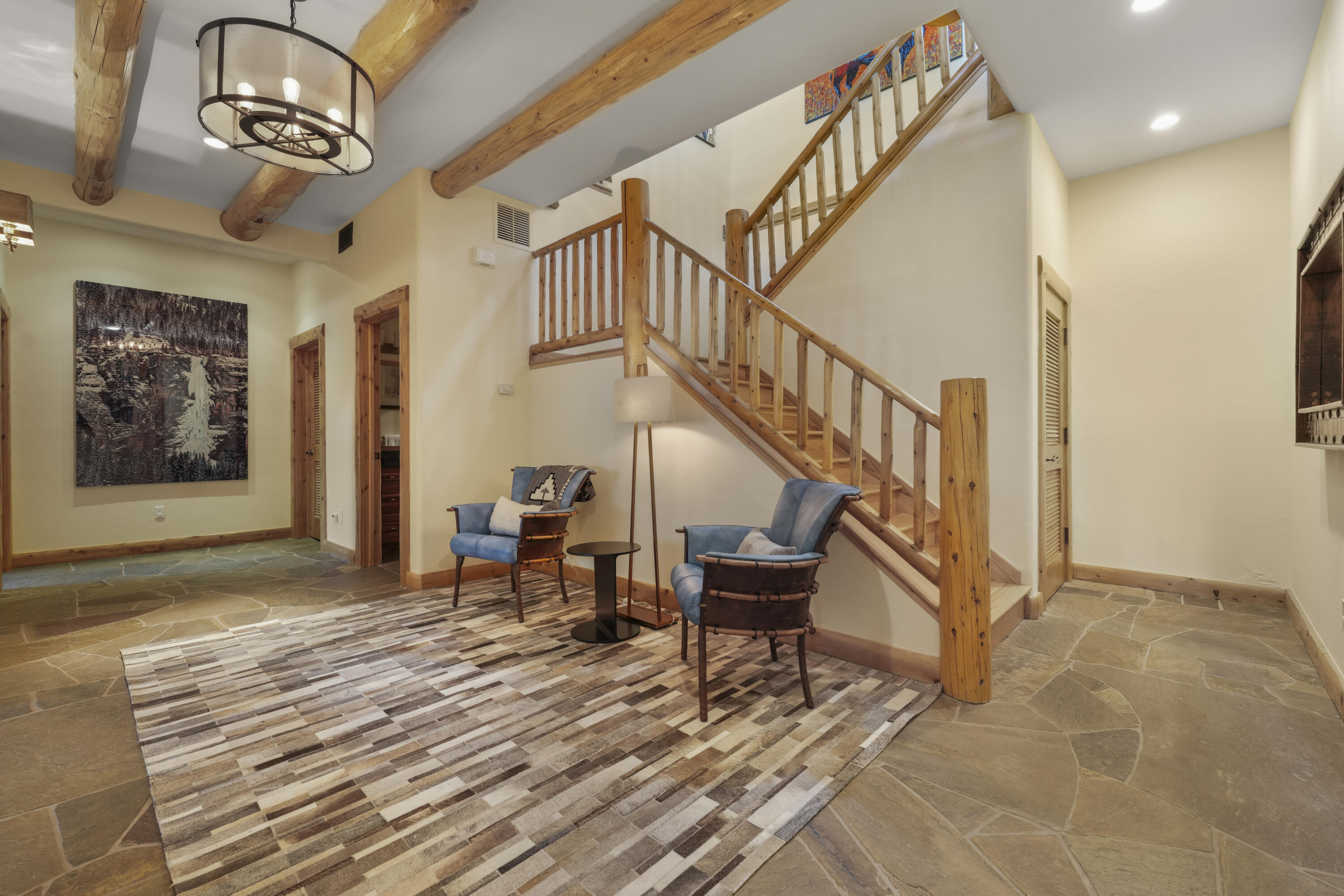 Furnished entryway with a wooden staircase, exposed beams, and two blue chairs.