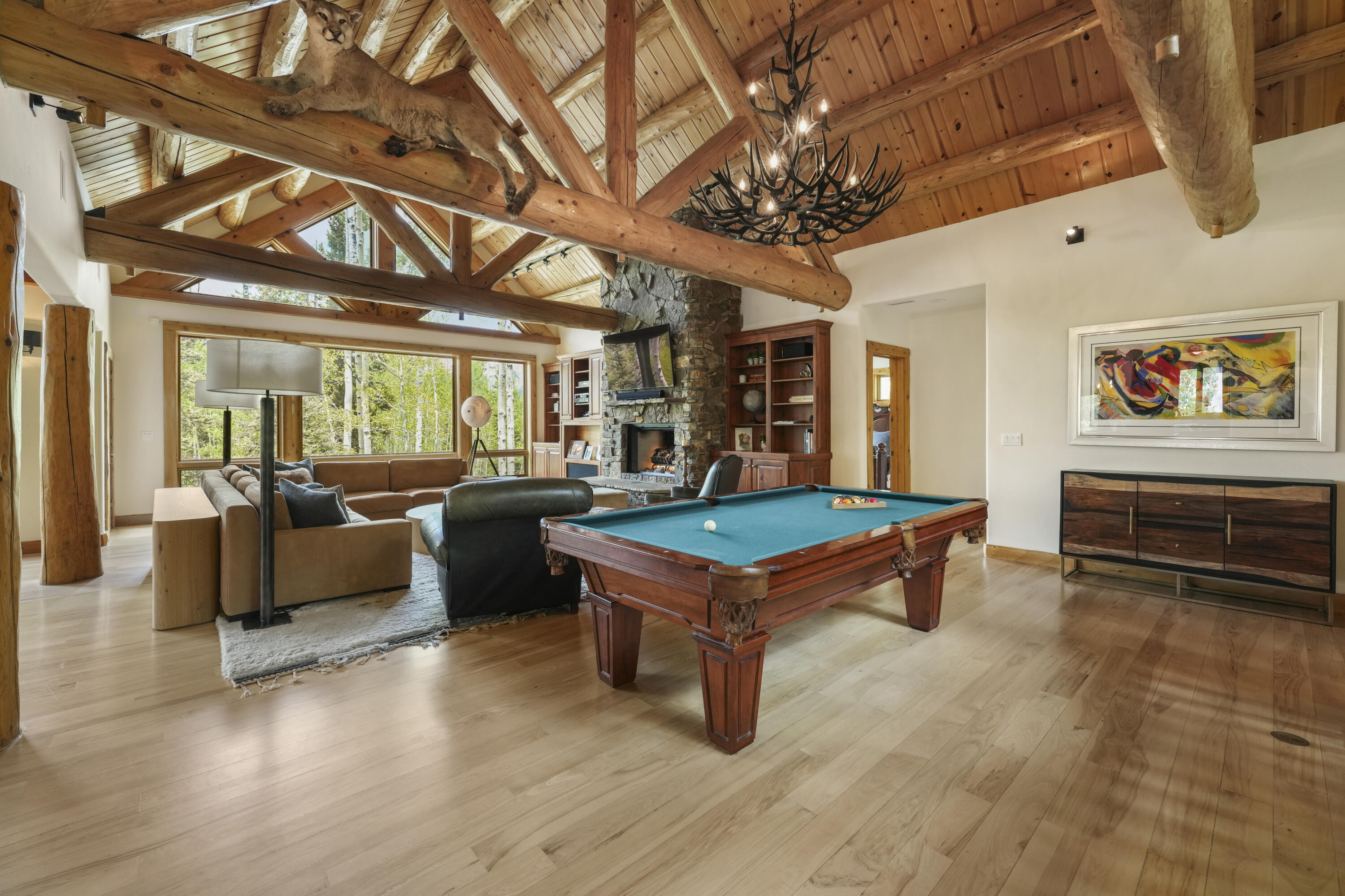 Living and game room with a pool table, stone fireplace, and vaulted timber-beam ceiling.