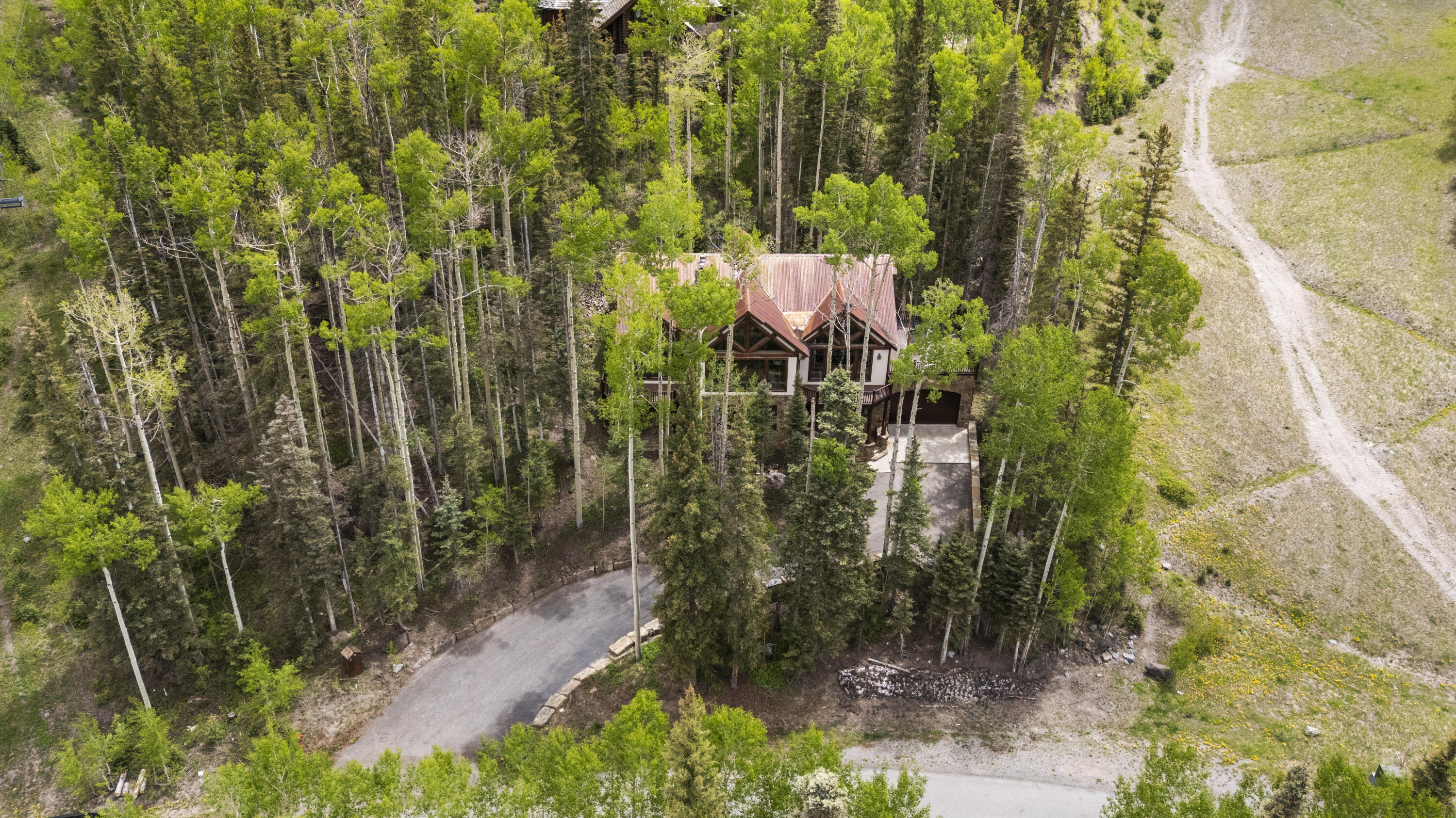 Aerial view of a mountain home nestled among trees beside a grassy ski slope.