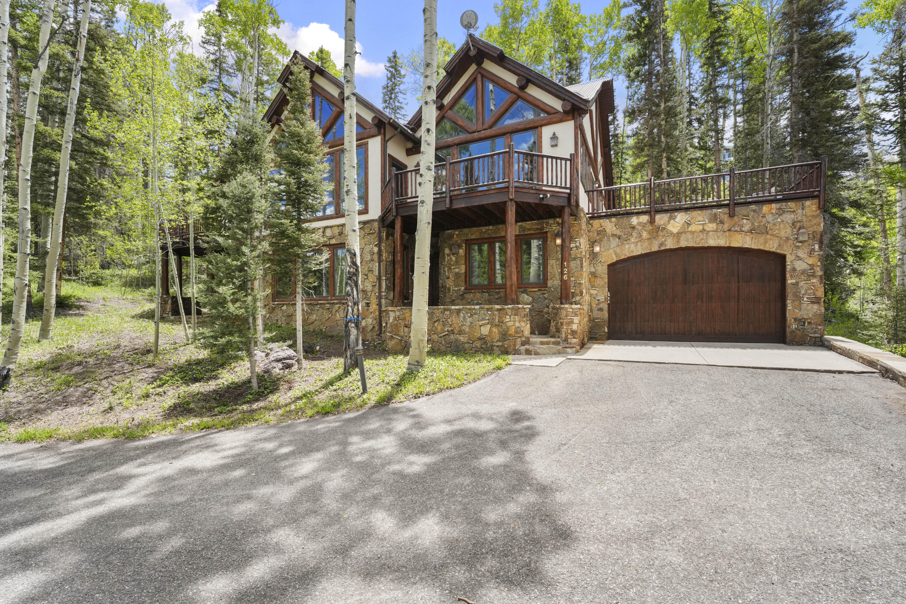 Stone-and-timber mountain home with a raised balcony and garage among aspen trees.