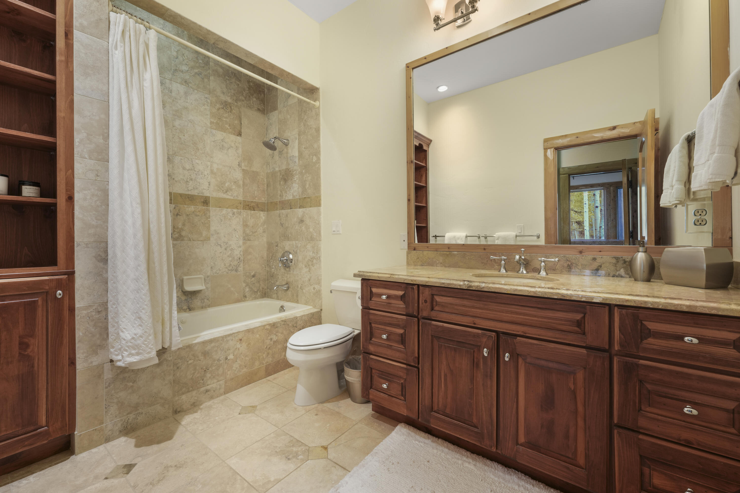 Bathroom with a tiled tub and shower, dark wood vanity, stone countertop, and large mirror.