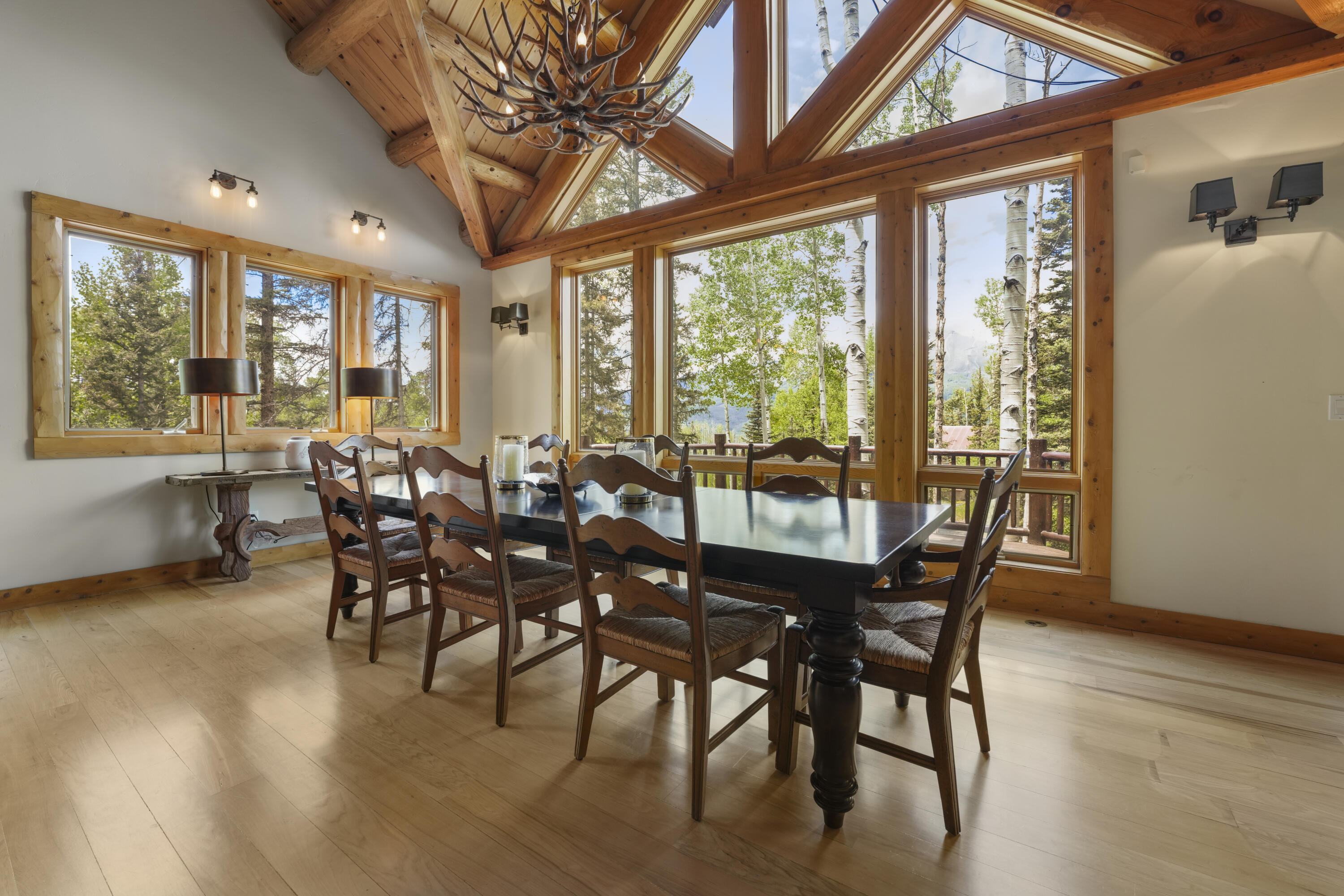 Dining room with a vaulted timber ceiling, long table, and large windows overlooking trees and mountains.