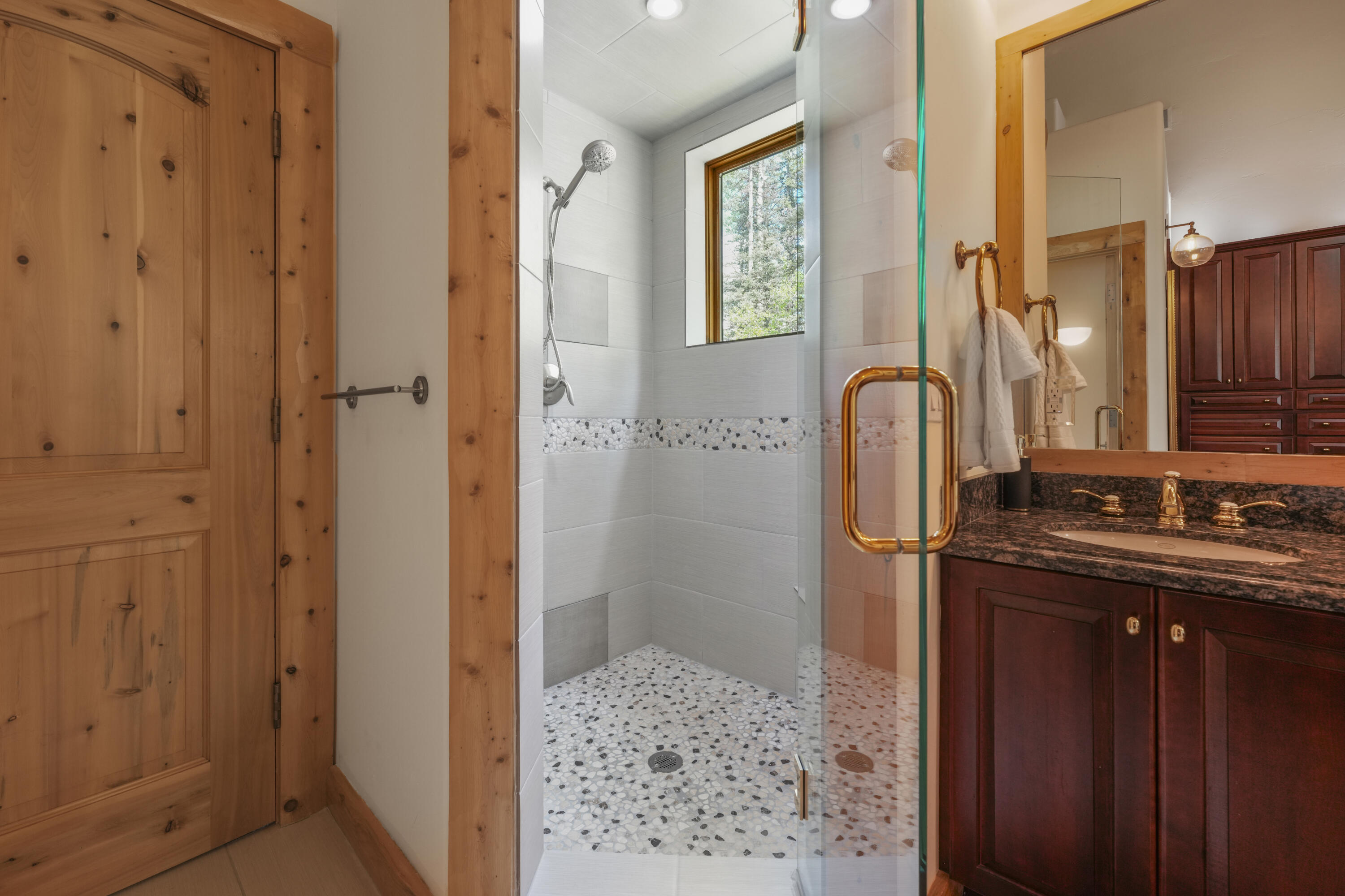 Bathroom with glass-enclosed walk-in shower, pebble tile floor, and dark wood vanity.