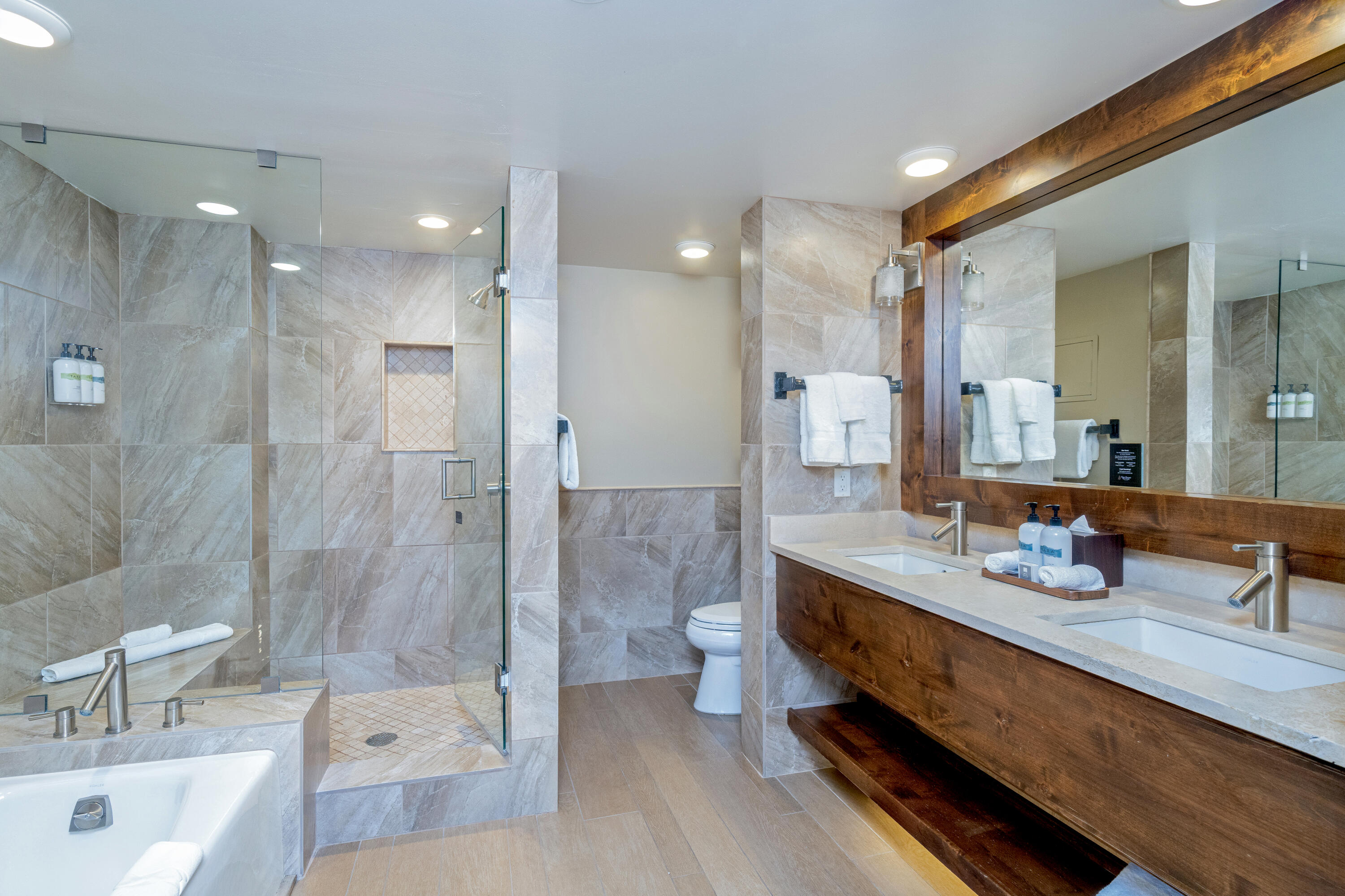 Bathroom with a glass shower, built-in tub, and double vanity beneath a large wood-framed mirror.
