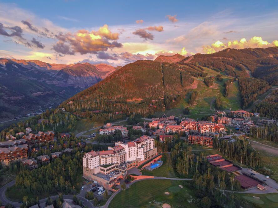 Aerial view of a mountain resort village beneath forested slopes at sunset.