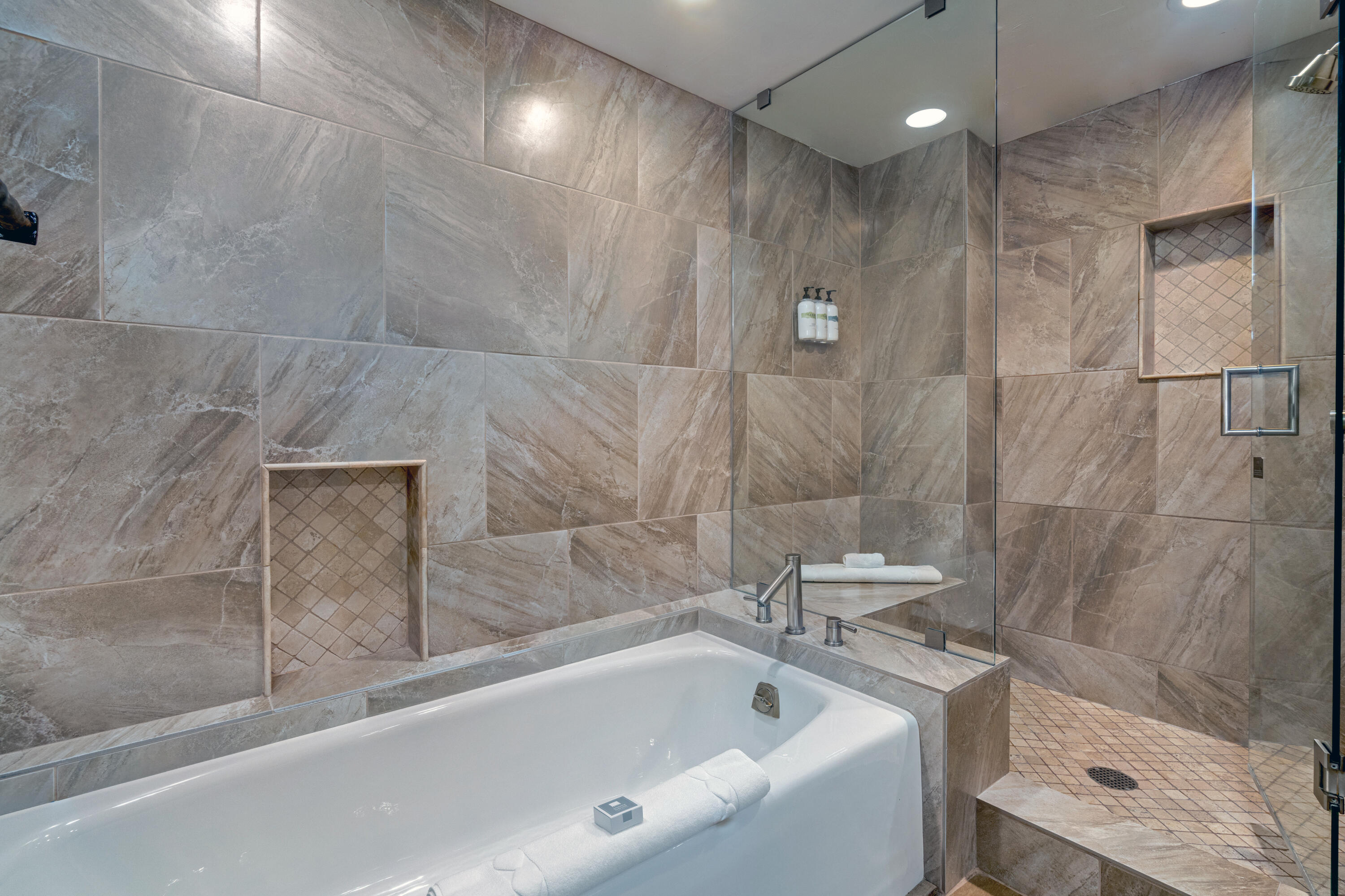 Bathroom with a white soaking tub, glass shower, and gray stone-look tile.