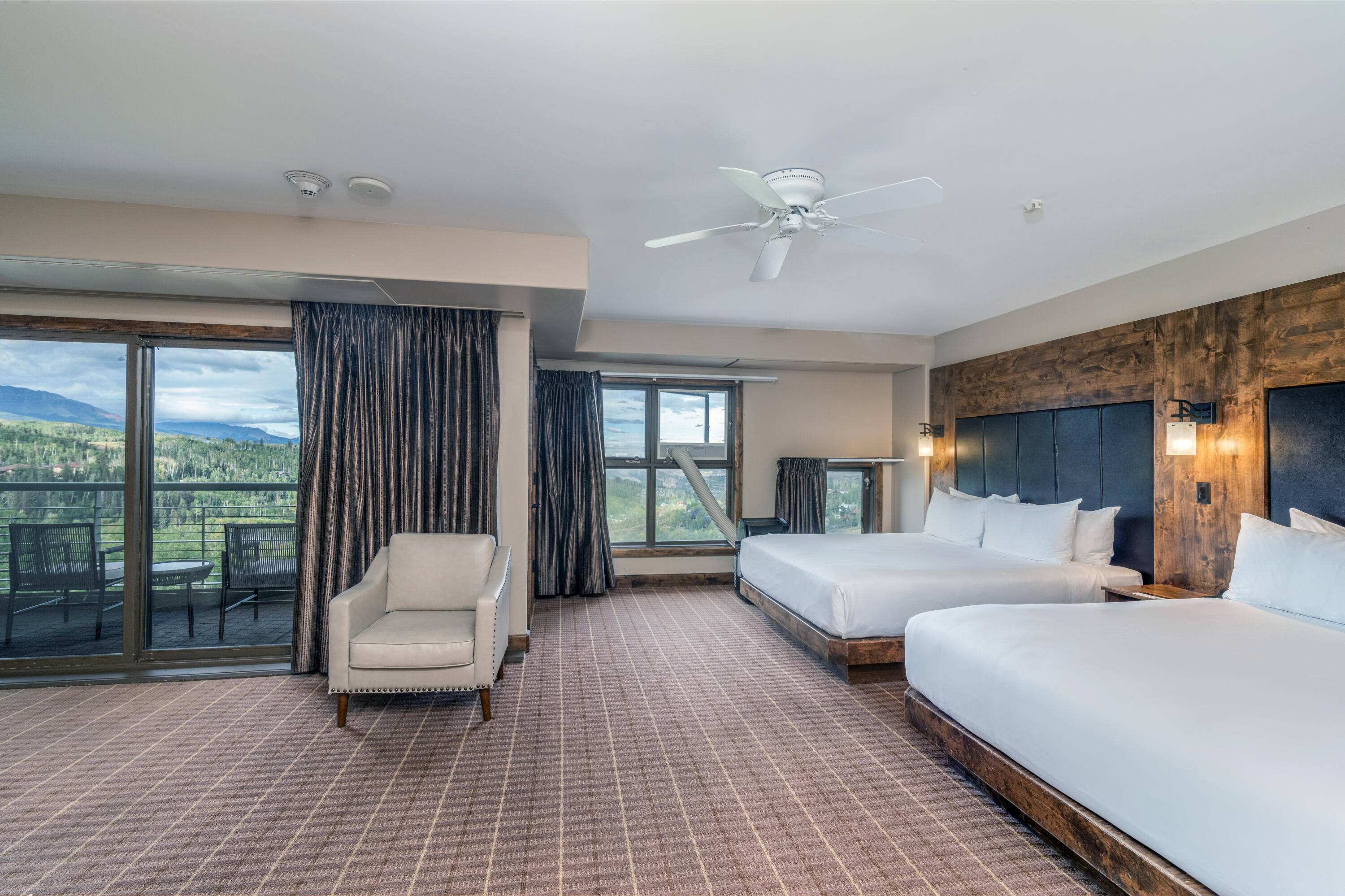Bedroom with two beds and a balcony overlooking forested mountains.