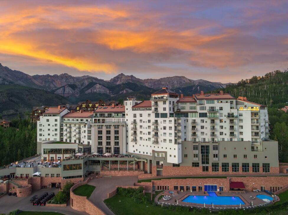Mountain resort condominium with balconies and a pool beneath colorful sunset clouds.