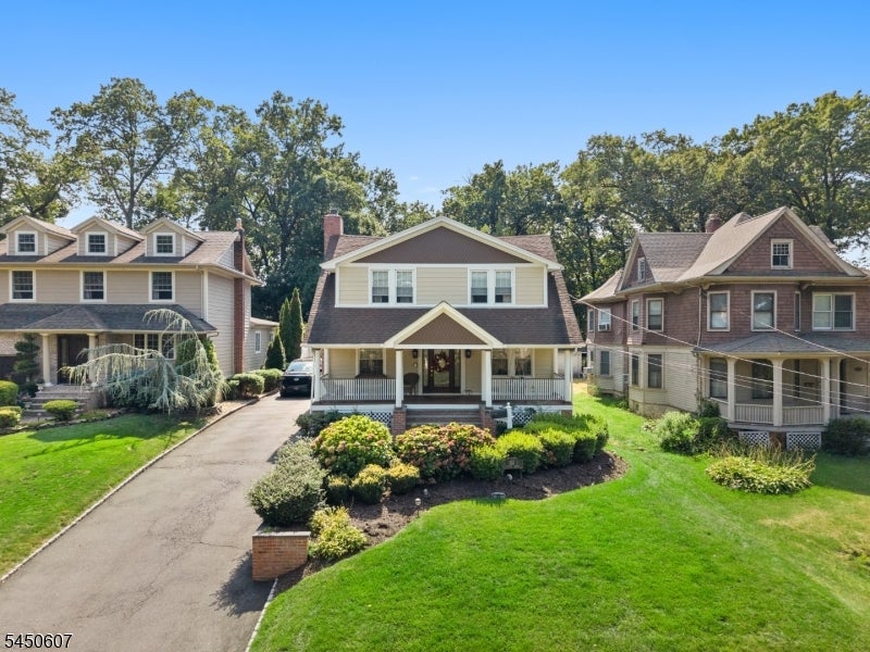 Two-story house with a covered porch, landscaped garden beds, and driveway between neighboring homes.