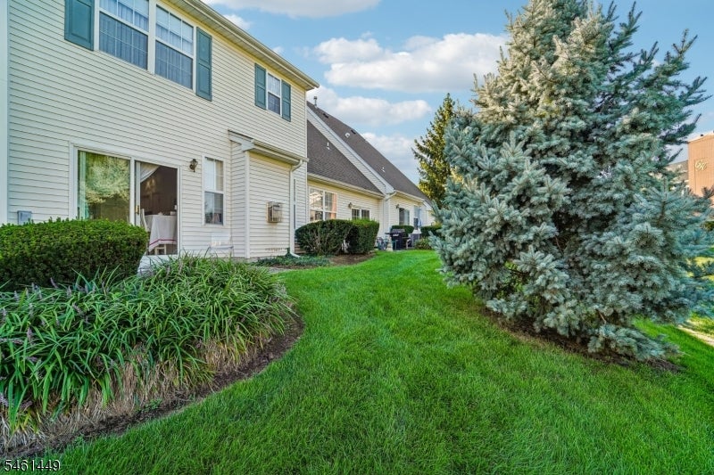Side exterior of a light-sided home beside a broad lawn and large evergreen tree.