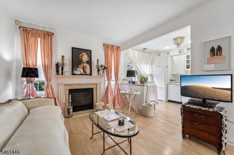 Living room with a fireplace, cream sofa, peach curtains, and an adjoining white kitchen.