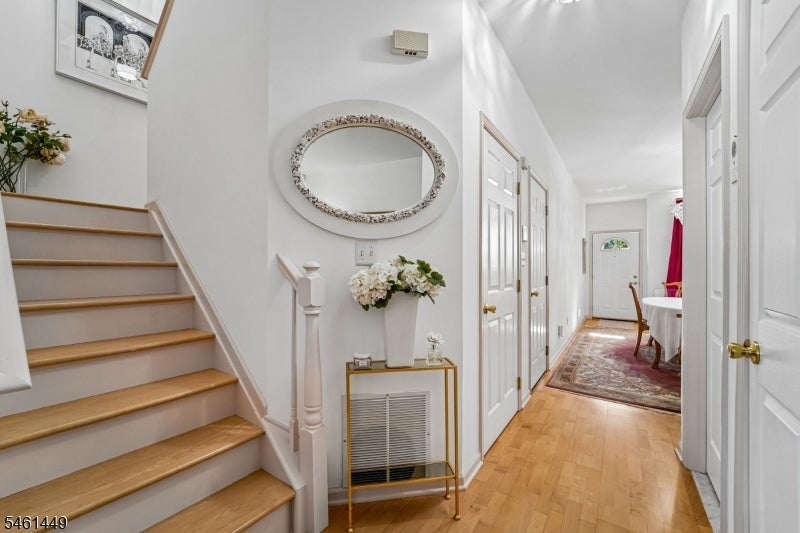 Hallway with a wood staircase, oval mirror, and runner leading to the front door.