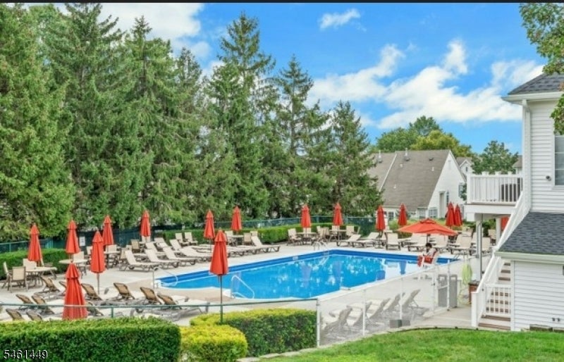 Community swimming pool with lounge chairs and red umbrellas beside white-sided buildings.