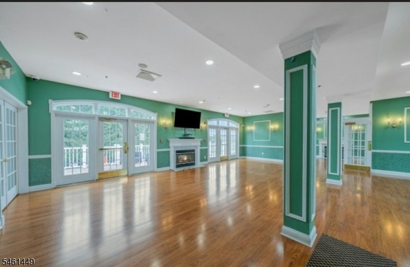 Spacious green-walled room with a fireplace, polished wood floors, and tall glass doors.
