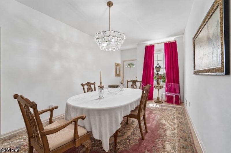 Dining room with a white-clothed round table, carved wooden chairs, chandelier, and magenta curtains.
