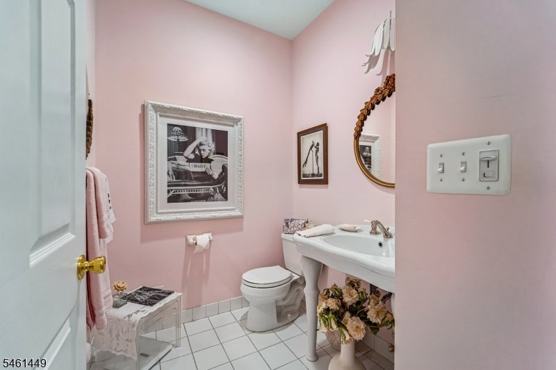 Pink bathroom with a pedestal sink, toilet, ornate mirror, and framed wall art.