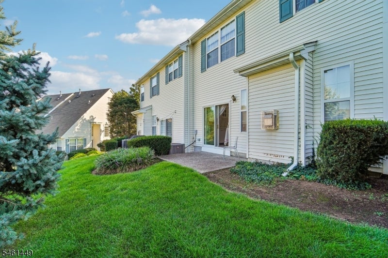 Two-story townhouse with a small patio, green lawn, shrubs, and an evergreen tree.