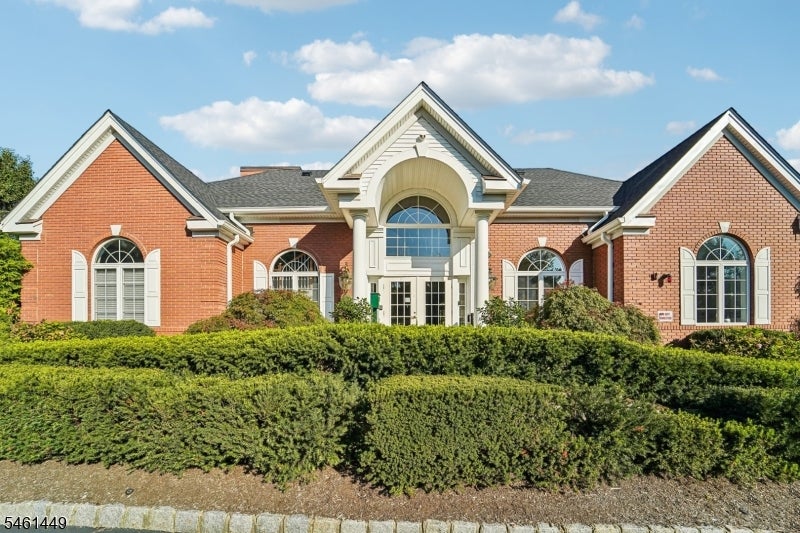Red-brick building with a central arched entrance, white trim, and a tall hedge.