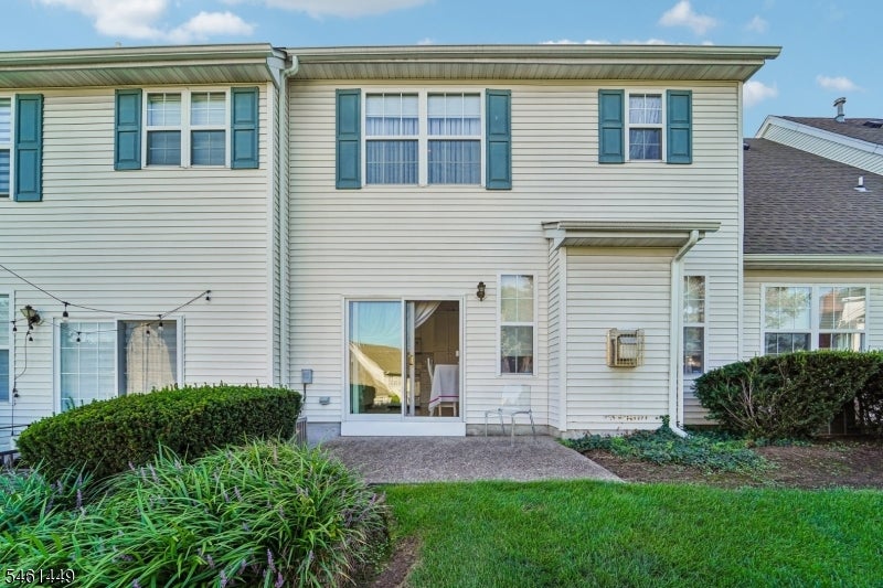 Rear of a two-story attached home with teal shutters, sliding glass door, and shrub-bordered patio.