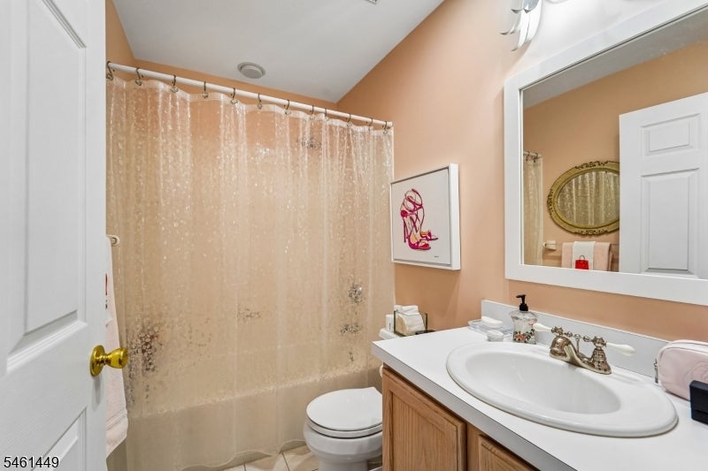 Bathroom with a patterned shower curtain, white sink, wood vanity, and large mirror.