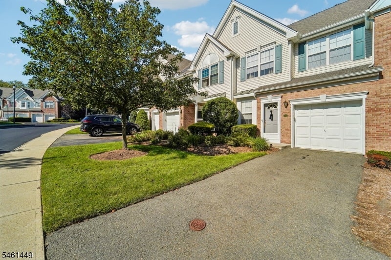 Townhouse exterior with attached garages, a broad driveway, landscaped lawn, and mature tree.