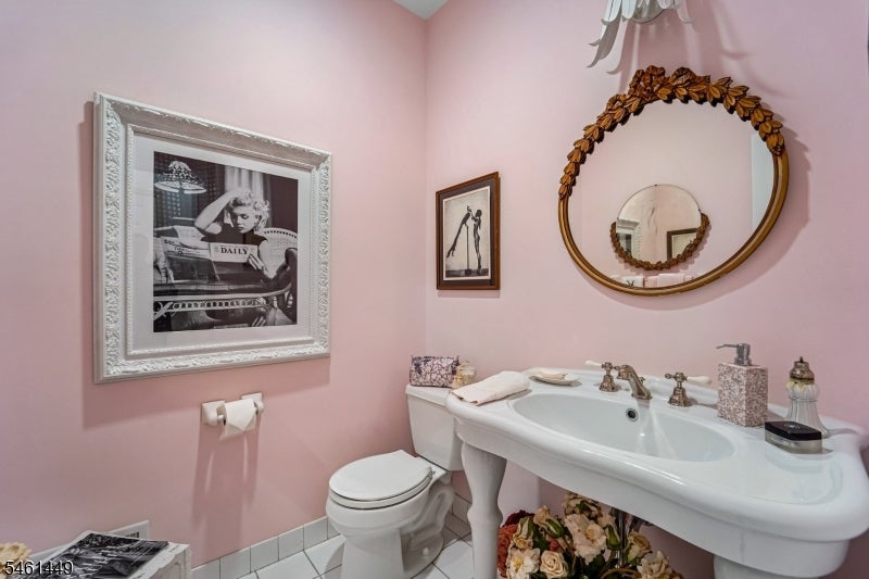 Pink bathroom with a white pedestal sink, toilet, and ornate oval mirror.