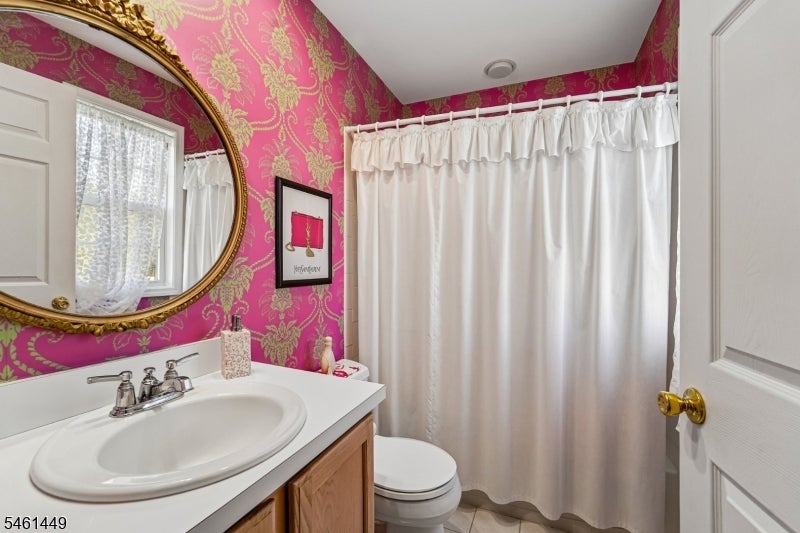 Bathroom with pink-and-gold patterned walls, an ornate oval mirror, and a white vanity.