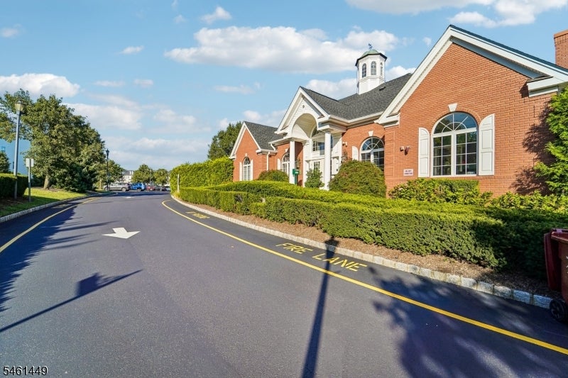 Red-brick building with arched windows beside a curved driveway and low hedges.