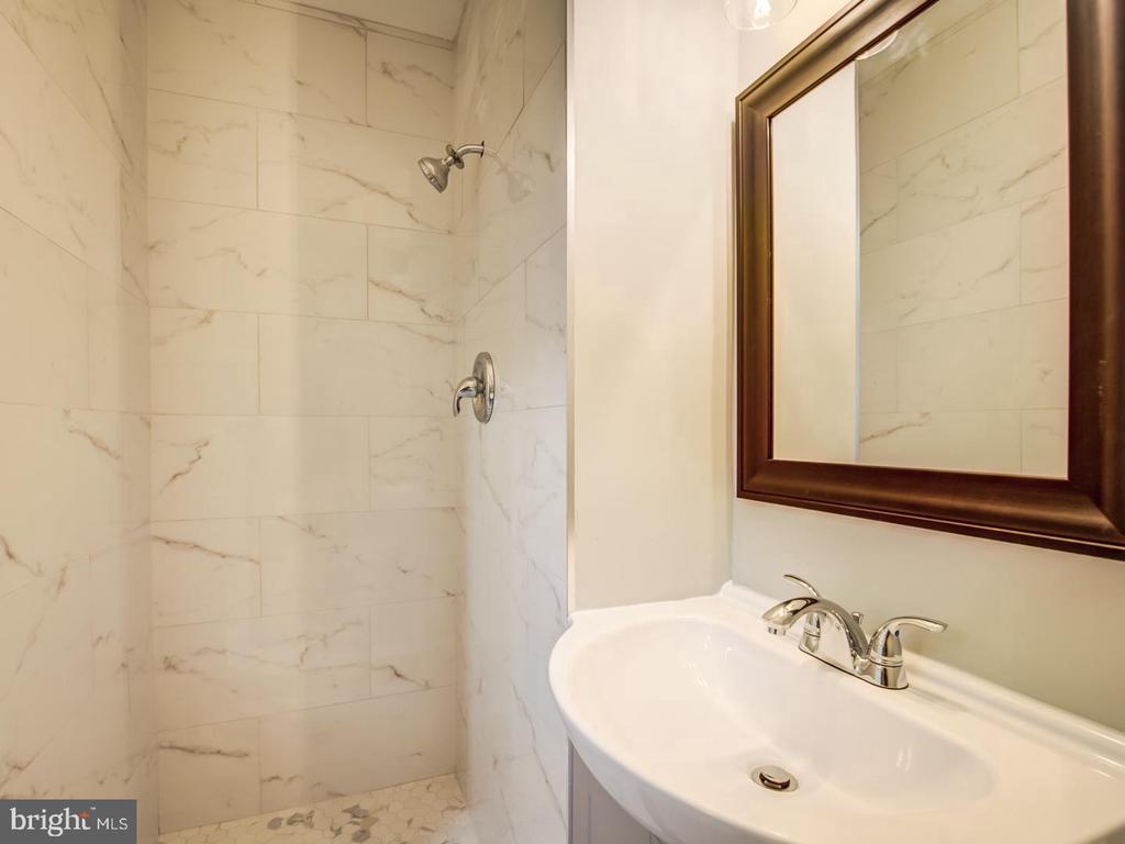 Bathroom with a marble-look tiled shower, white sink, chrome fixtures, and dark wood-framed mirror.