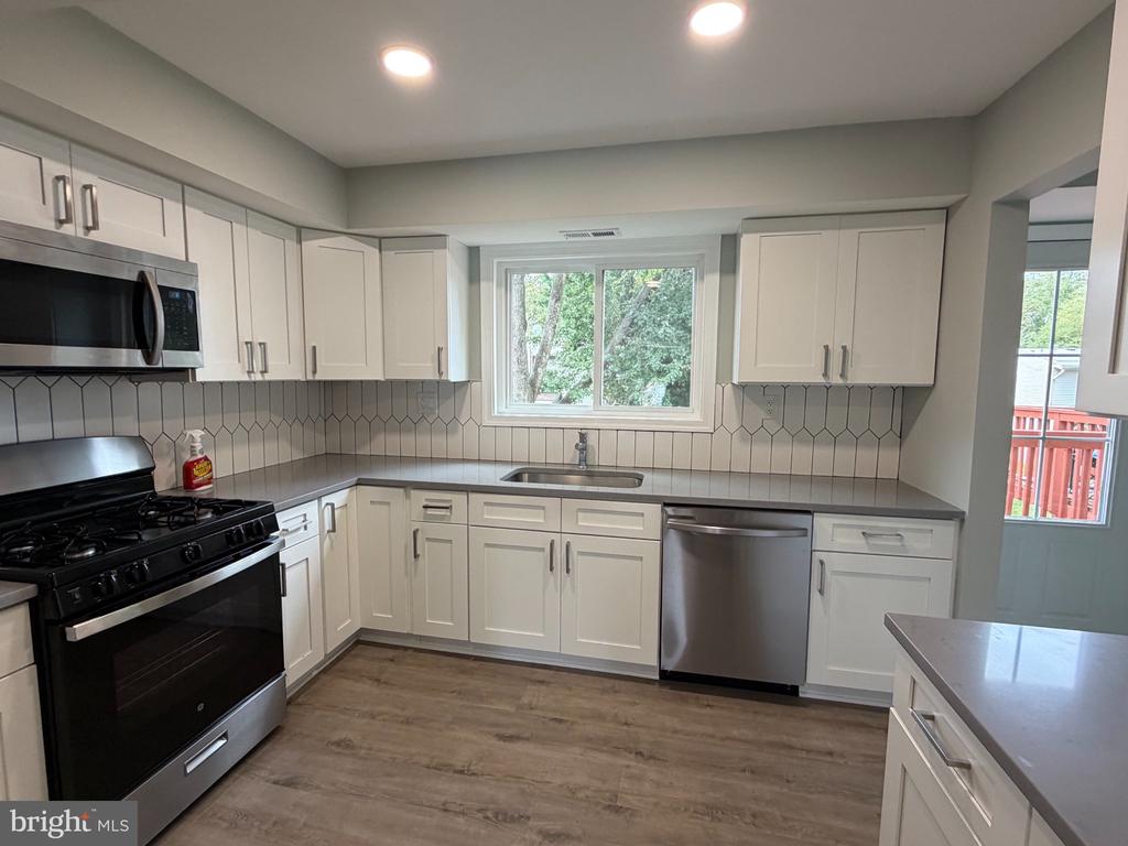 Kitchen with white cabinets, geometric tile backsplash, stainless appliances, and a window overlooking trees.