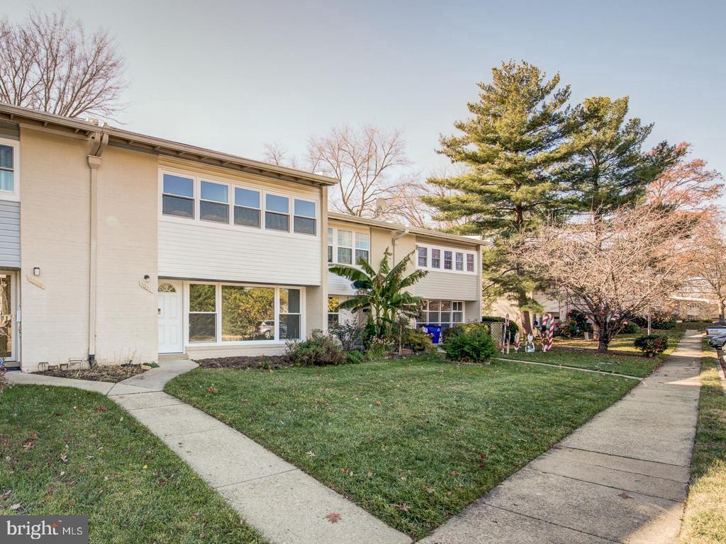 Two-story attached home with light siding, a front lawn, and mature trees.
