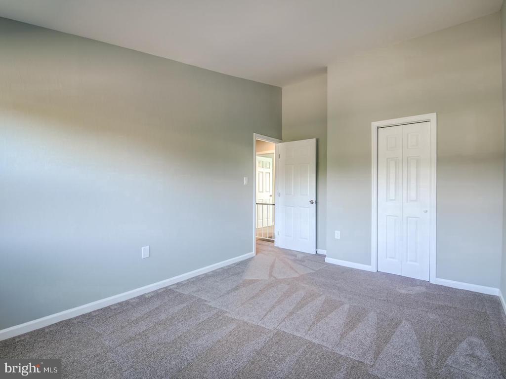 Empty bedroom with patterned beige carpet, gray-green walls, and a white double-door closet.
