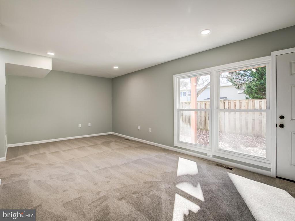 Empty carpeted room with gray walls, large windows, and a door to the fenced yard.