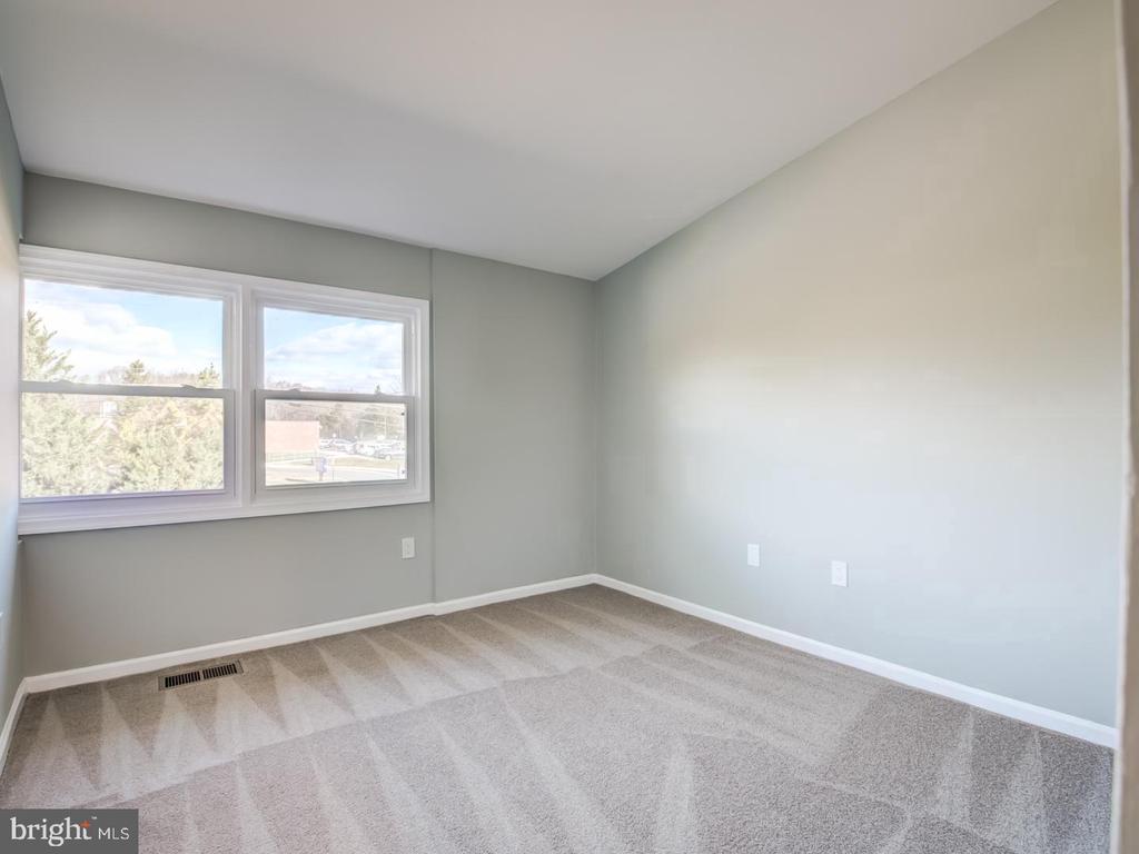 Vacant bedroom with beige patterned carpet and two side-by-side windows.