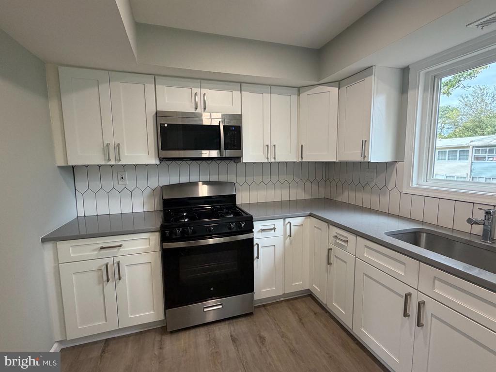 Kitchen with white shaker cabinets, geometric tile backsplash, and black gas range.