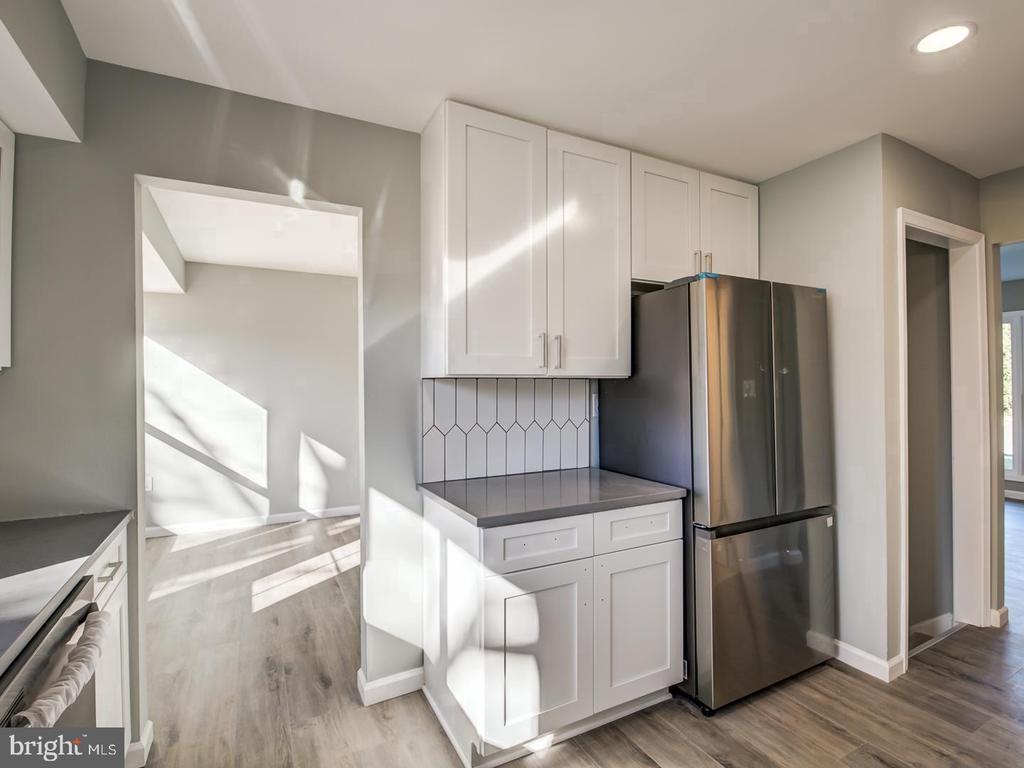 Renovated kitchen with white cabinets, geometric tile backsplash, and stainless steel refrigerator.