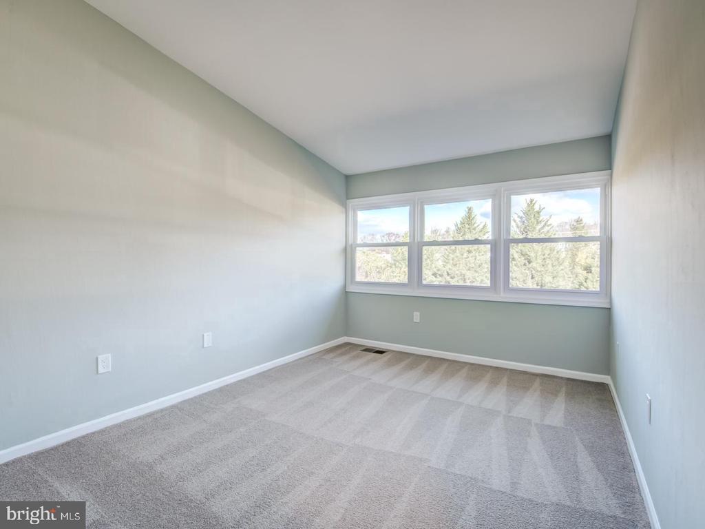 Empty bedroom with gray carpet and wide windows overlooking trees.