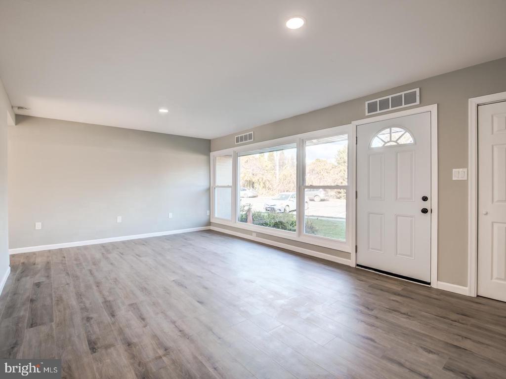 Vacant living room with gray flooring, large front windows, and a white entry door.
