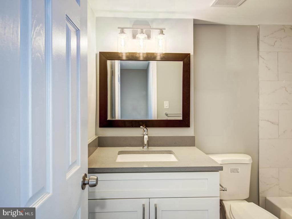 Bathroom with a white vanity, dark-framed mirror, and marble-look tiled tub surround.
