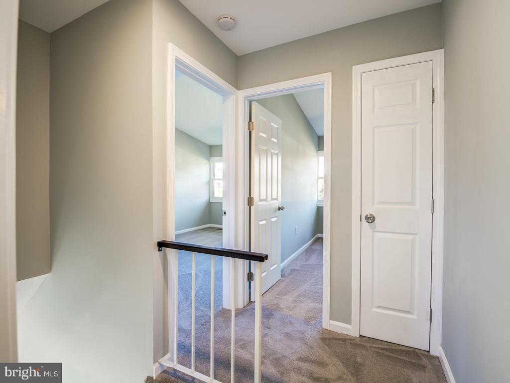 Carpeted upstairs landing with a white railing and doorways into empty rooms.