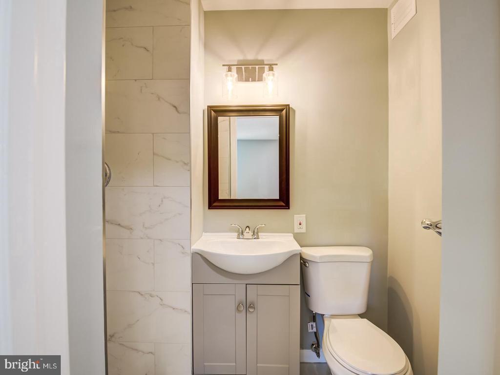 Bathroom with a gray vanity, framed mirror, toilet, and marble-look tiled shower wall.