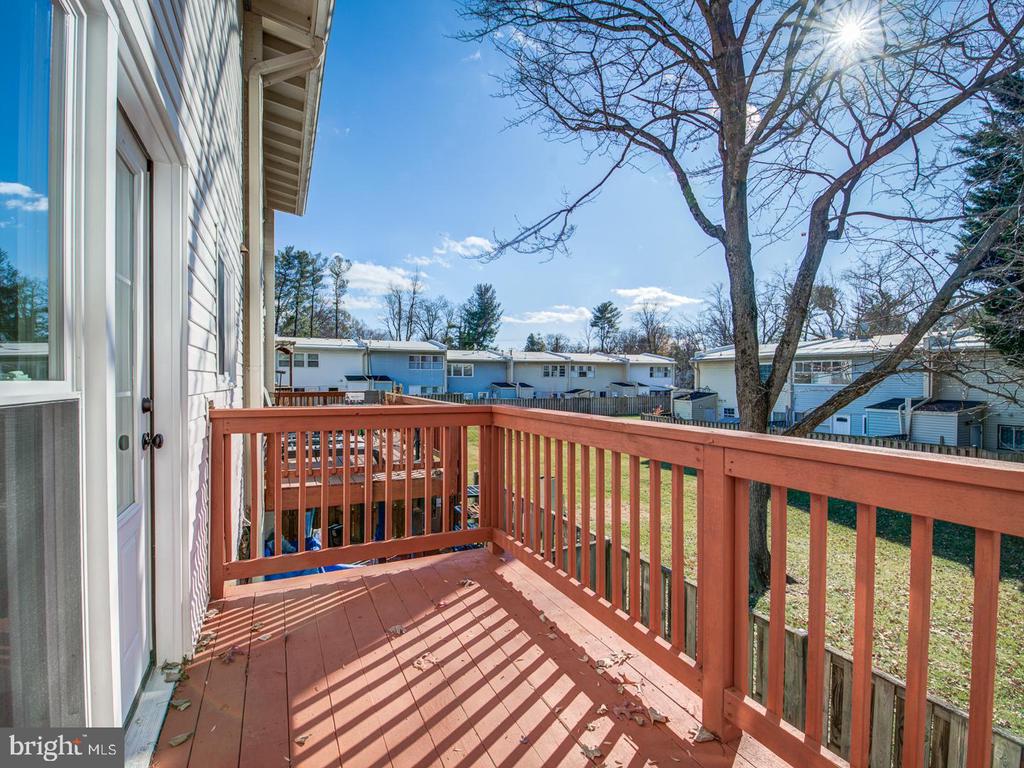 Red wooden deck with matching railings overlooking neighboring homes and a grassy yard.