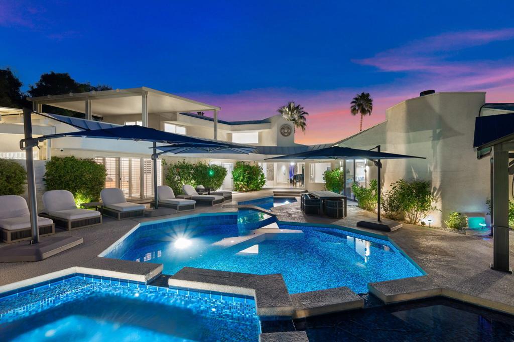 Modern Palm Springs home with an angular illuminated pool and outdoor lounge seating at dusk.