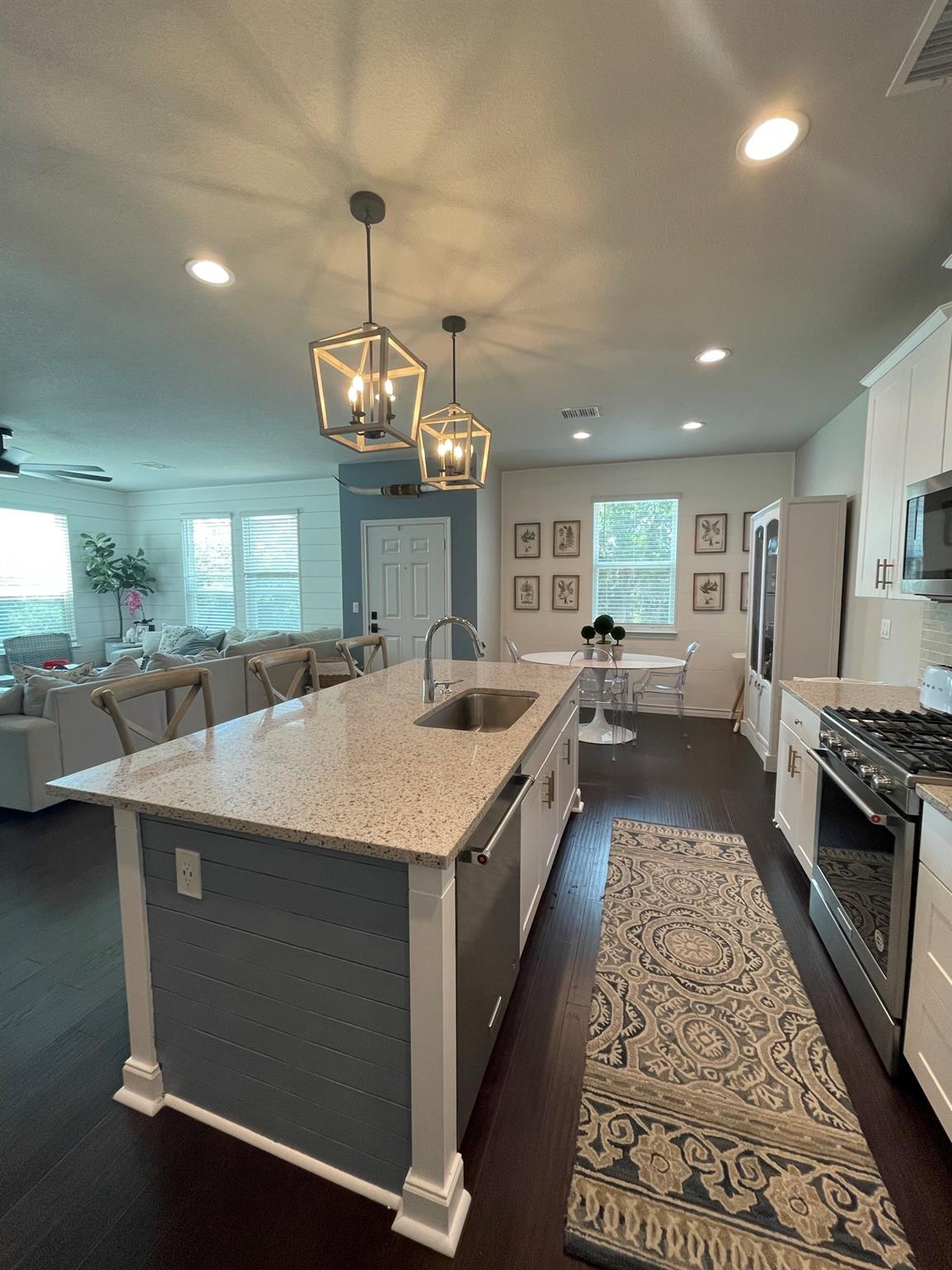 Open-plan kitchen with a large gray island, speckled countertops, geometric pendant lights, and adjoining living area.