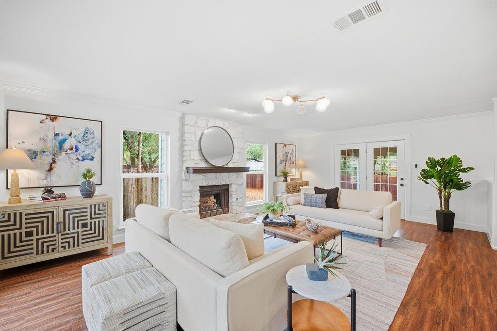 Living room with white sofas, a stone fireplace, round mirror, and hardwood floors.