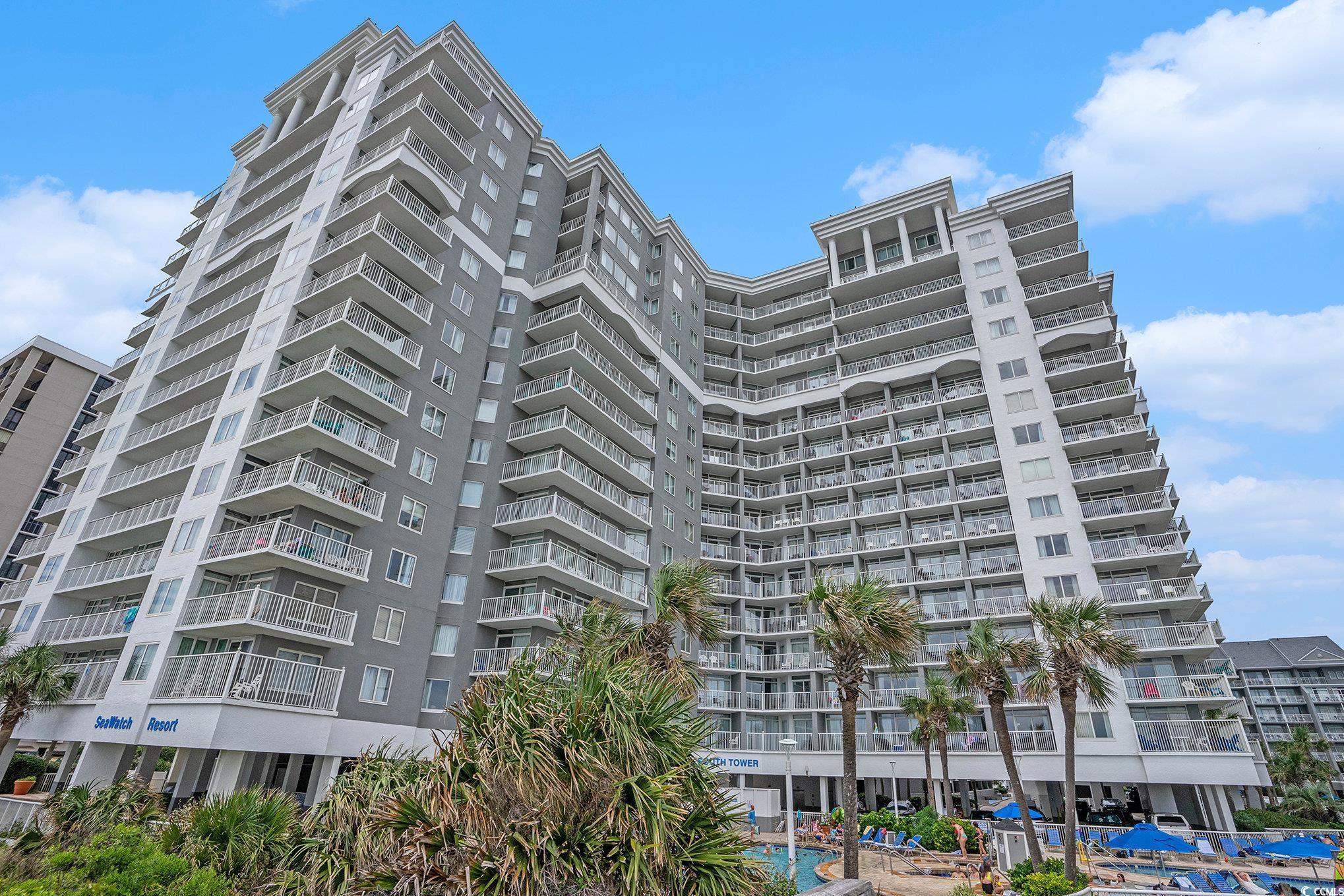 SeaWatch Resort’s high-rise exterior with balconies, palm trees, and a pool.