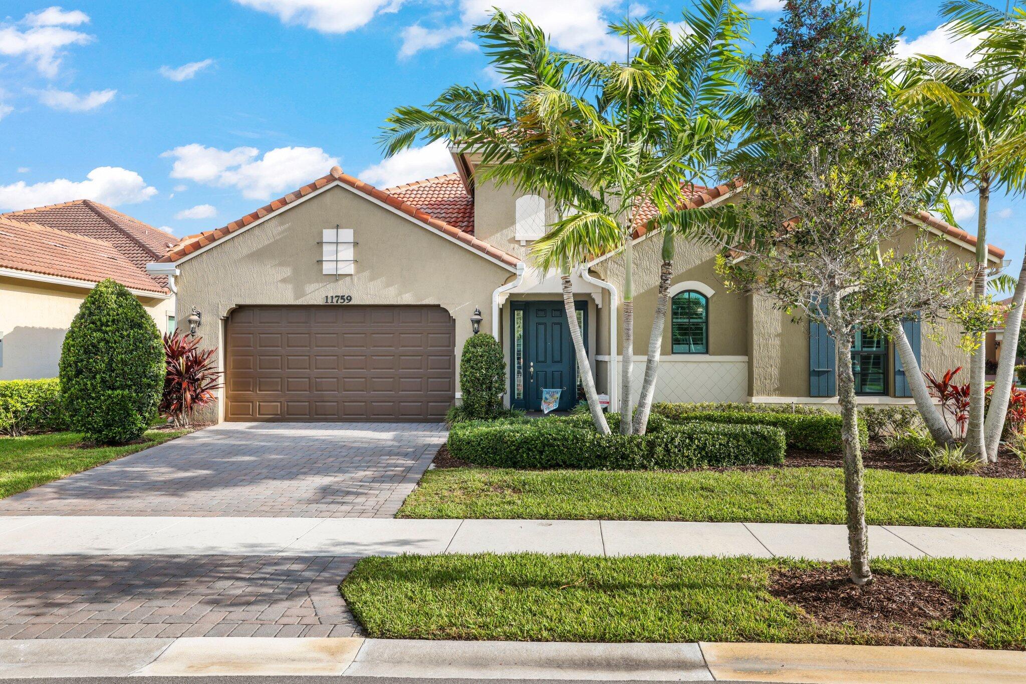 Tan stucco home with terracotta roof, blue entry door, paver driveway, and palm trees.